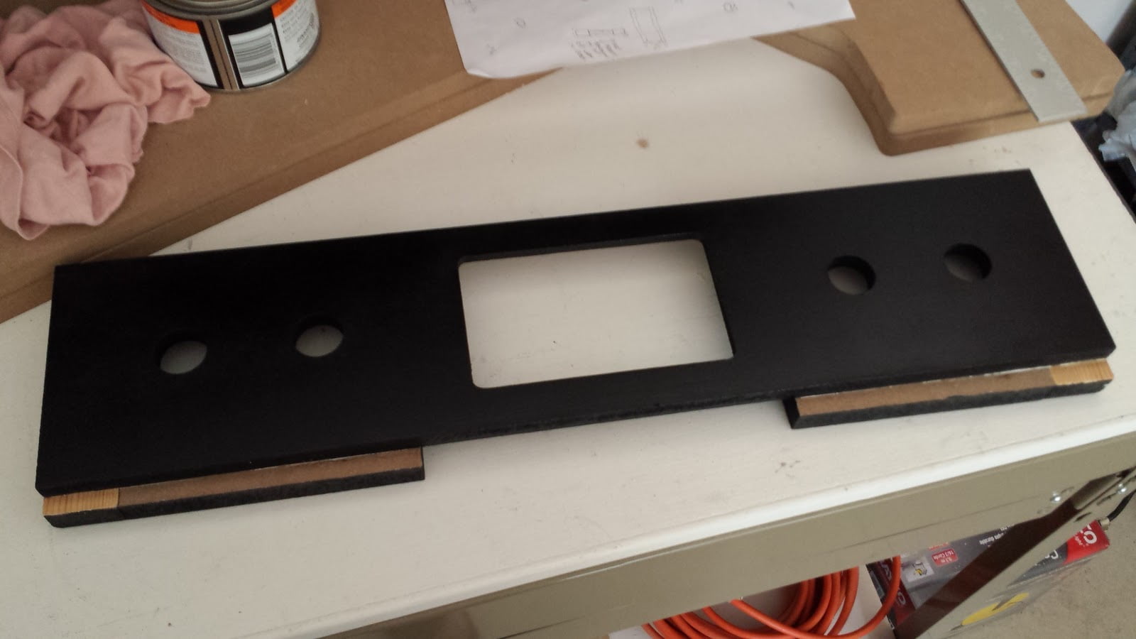 Administration panel painted black. Painters tape has been removed from the furring strip on the bottom, revealing unfinished MDF material.