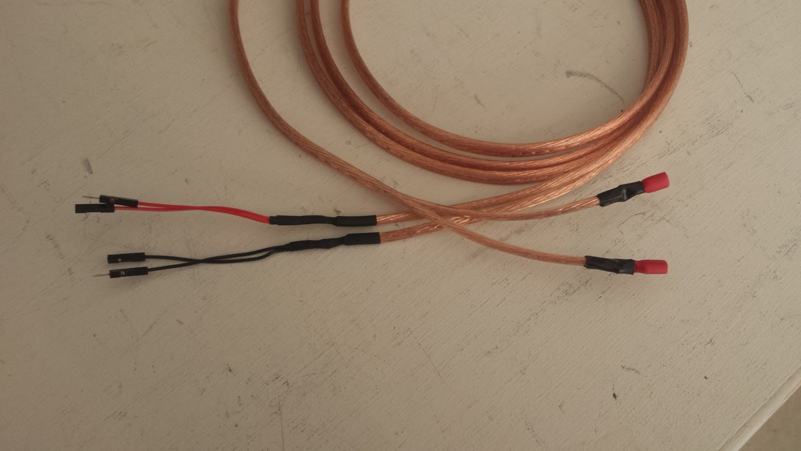 A length of speaker wire. On one end of each of the pair or wires, male & female patch panel wire has been soldered. On the other end of each wire, a terminal connector is soldered in place.