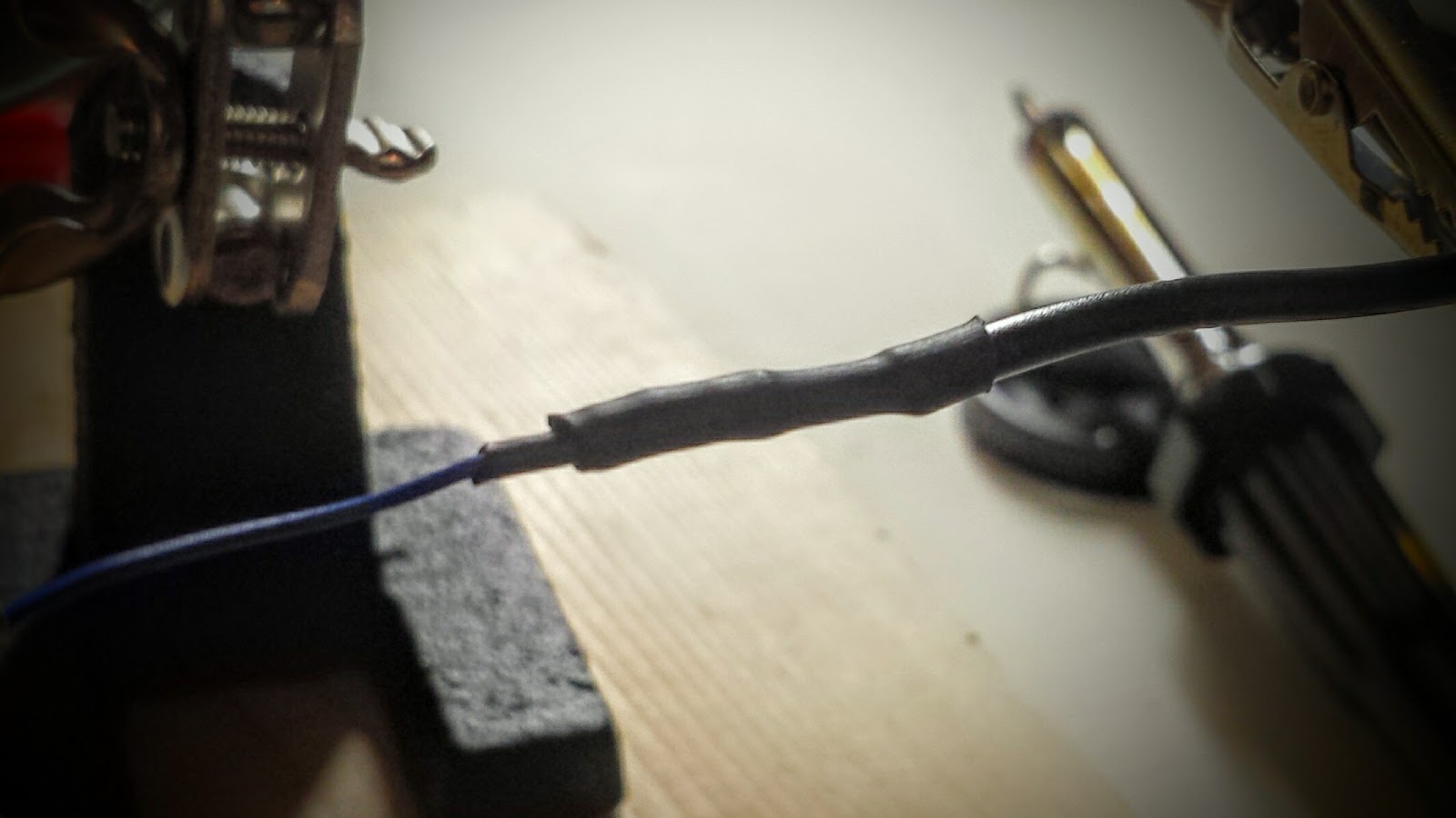 Close up of a thin wire, soldered to a thicker wire. A small length of heat-shrink tubing is attached to the thinner wire, giving that wire sufficient diameter to make it possible for a second heat-shrink to bridge the solder between both wires.